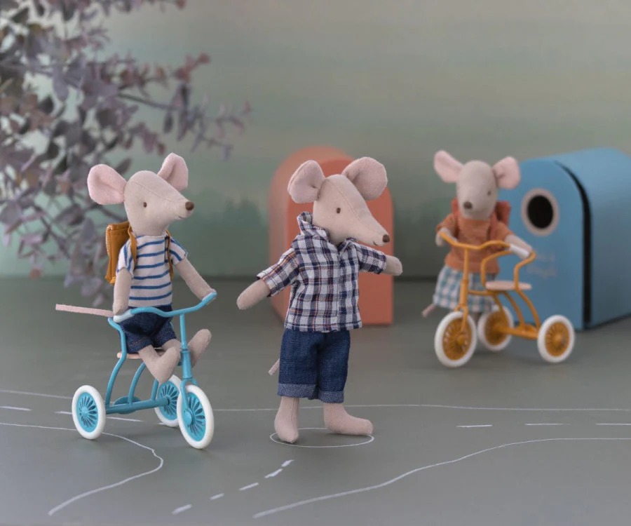 Three fabric mouse dolls dressed in miniature clothes, with two riding toy bicycles and one standing, against a playful pastel background.