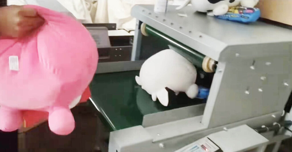 Soft plush toys being processed through a conveyor belt stuffing machine during toy manufacturing.