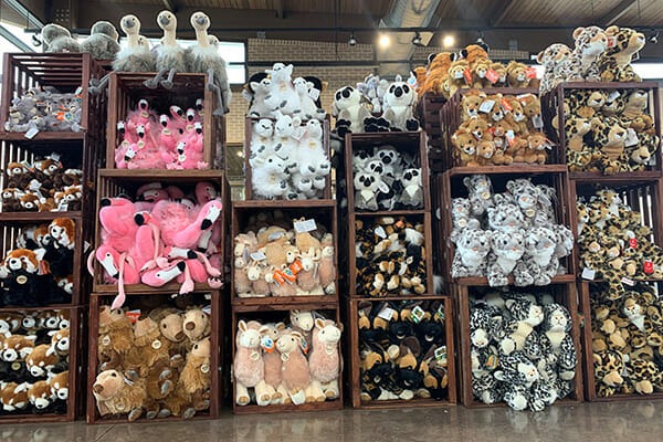 A large display of plush animal toys organized in wooden crates, featuring a variety of animals including flamingos, pandas, sloths, llamas, and more in different colors and sizes.