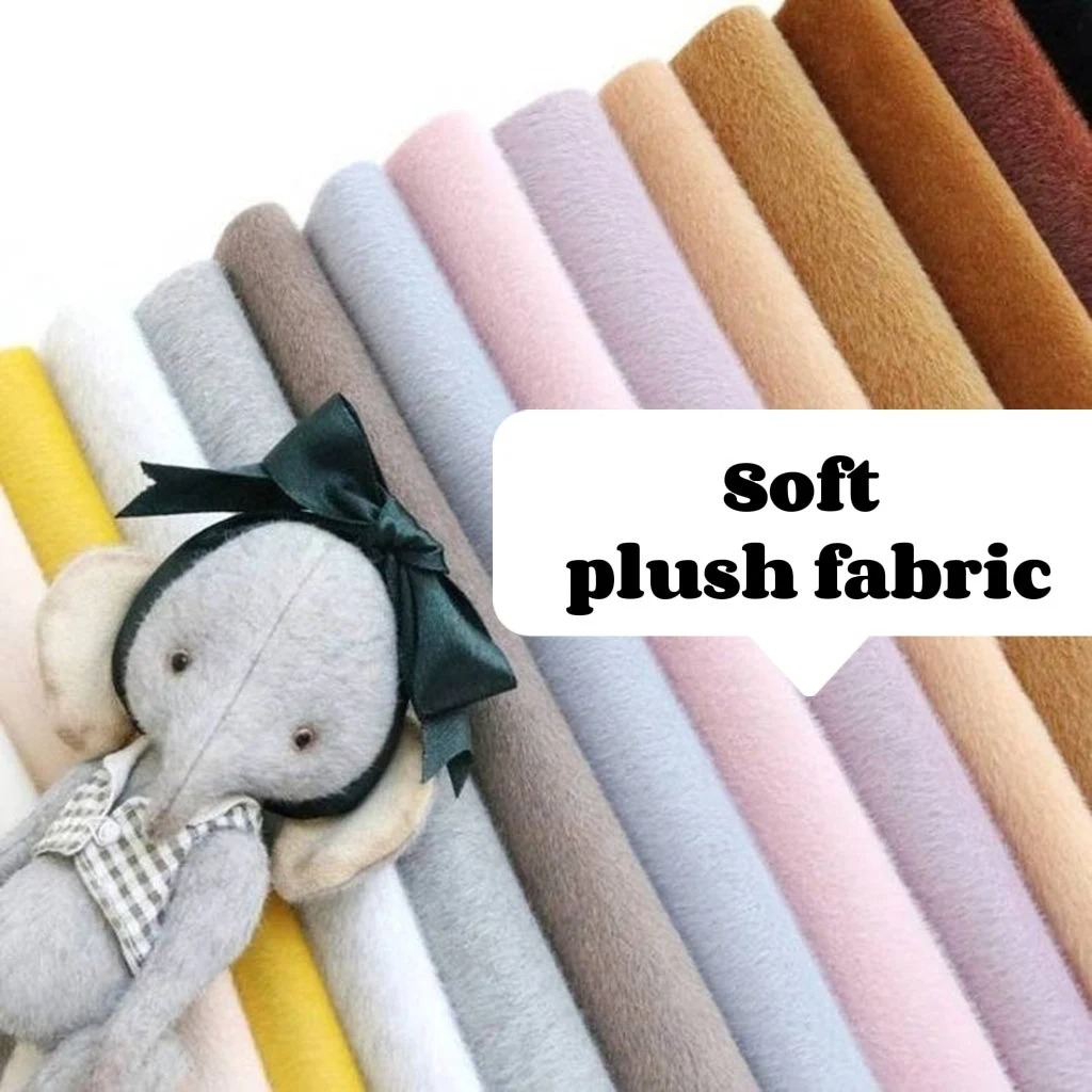 A variety of colorful soft plush fabric rolls displayed in a row with a handmade plush elephant toy wearing a bow and a checkered outfit, and a text label reading "Soft plush fabric."