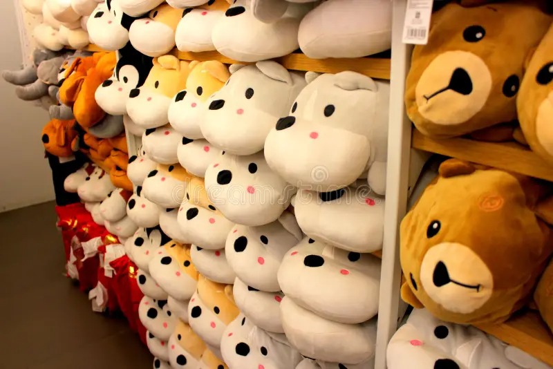 Shelves stacked with rows of plush animal head pillows in various colors and animal designs, including dogs, bears, and hippos, displayed in a store.