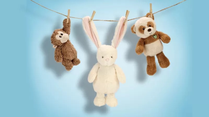 Three plush toys hanging from a clothesline against a blue background: a monkey, a white bunny, and a brown teddy bear.