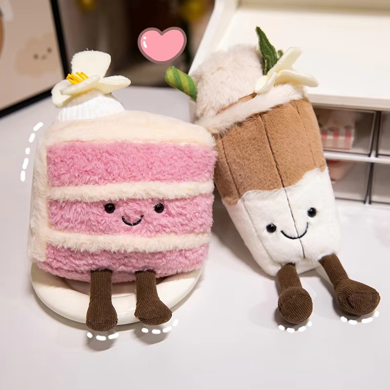 Two cute plush toys shaped like desserts with smiling faces and legs; one is a pink layer cake, the other resembles a brown and white drink topped with faux whipped cream and flowers.