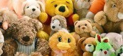 A colorful collection of various stuffed animals including a yellow duck, brown bears, a green bunny, a hedgehog, and a plush resembling Winnie the Pooh, all closely arranged together.