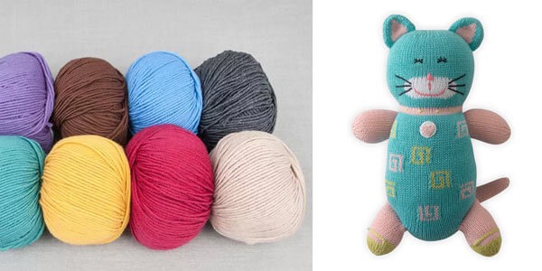 Colorful yarn balls arranged on the left and a finished knitted teal cat plush toy with pink limbs and embroidered details on the right.