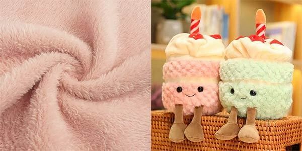 Close-up of soft pink plush fabric and two plush toys shaped like drinks with smiling faces, topped with whipped cream and straws in pastel pink and green.