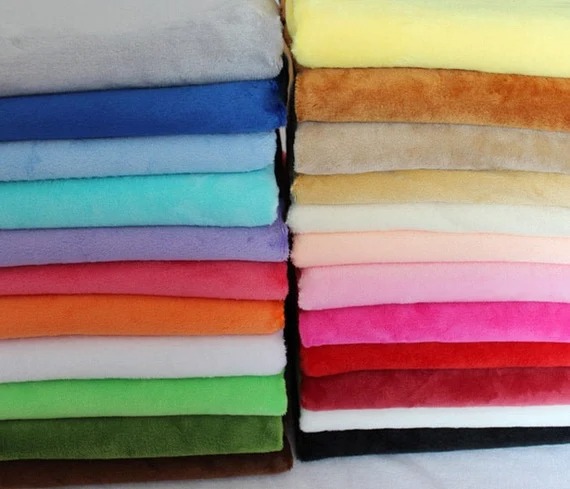 Neatly stacked colorful plush fabric sheets in various shades including blue, pink, green, and brown for sewing or crafting.
