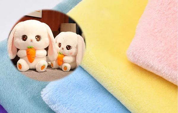 Soft colorful fleece fabric sheets in pastel tones with a circular inset showing two plush bunny toys holding carrots.