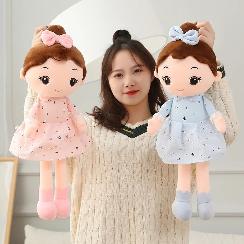 Woman holding two soft plush dolls wearing pink and blue dresses with matching bows.