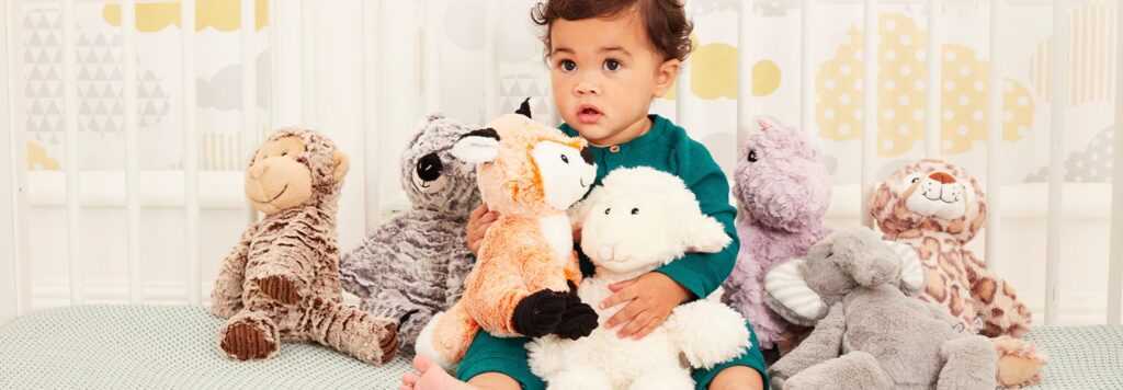 Baby sitting in crib surrounded by various plush stuffed animals including fox, lamb, elephant, and monkey.