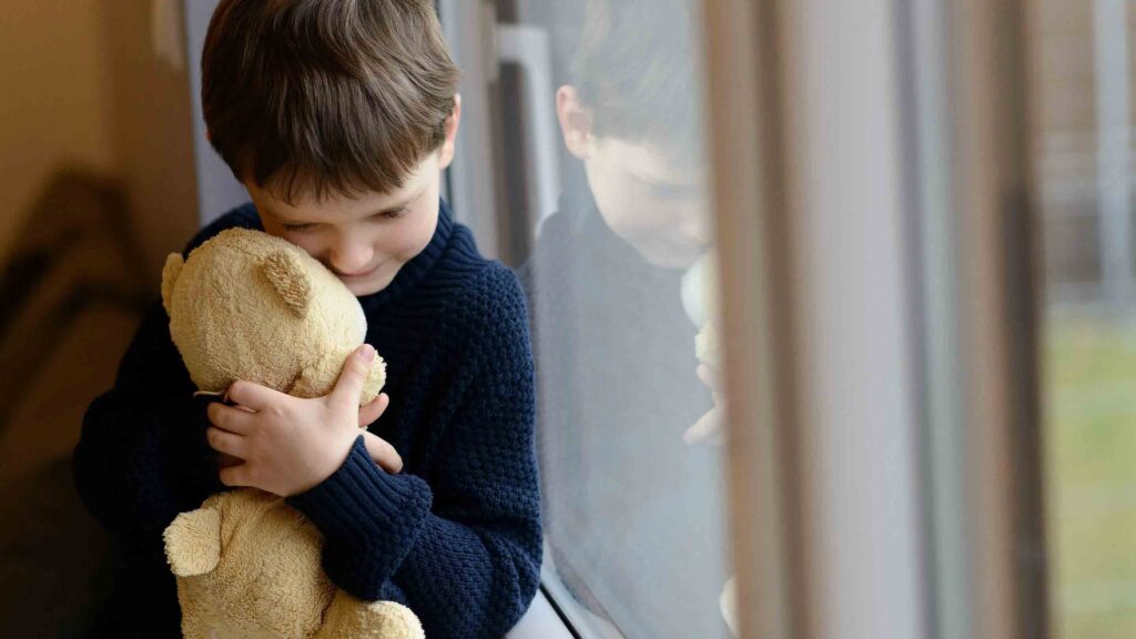 Boy hugging soft teddy bear by window
