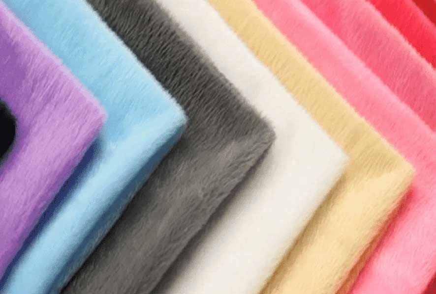 Soft plush fabrics in various colors including purple, blue, gray, white, beige, pink, and red, stacked diagonally.