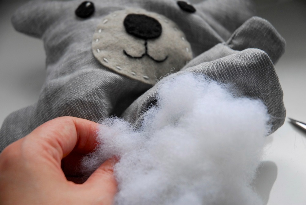 Riempimento a mano di un peluche di orso grigio con imbottitura in fibra di poliestere bianca durante il processo di fabbricazione del giocattolo.