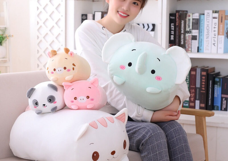 Girl holding soft pastel animal plush pillows including elephant, panda, pig, and cat.