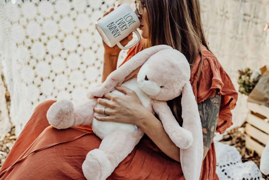 Donna che coccola un morbido coniglietto di peluche rosa mentre sorseggia un caffè