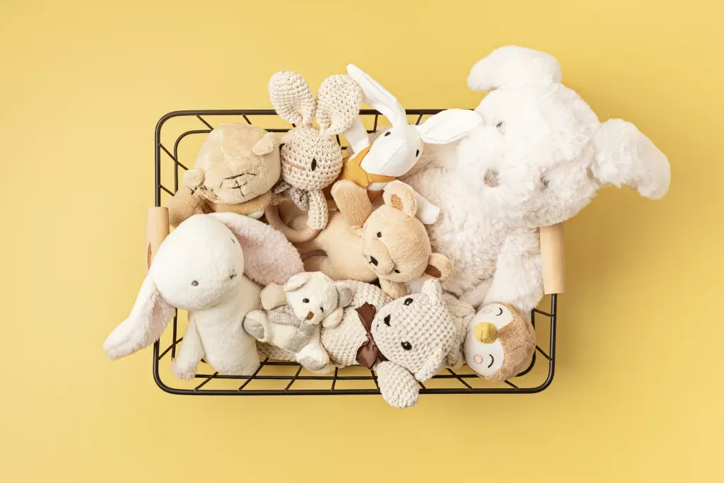 Assorted plush animal toys in a wire basket on yellow background.