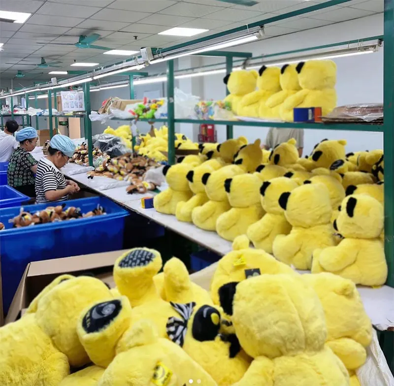 Factory workers assembling yellow plush toys lined up on shelves in a production facility.