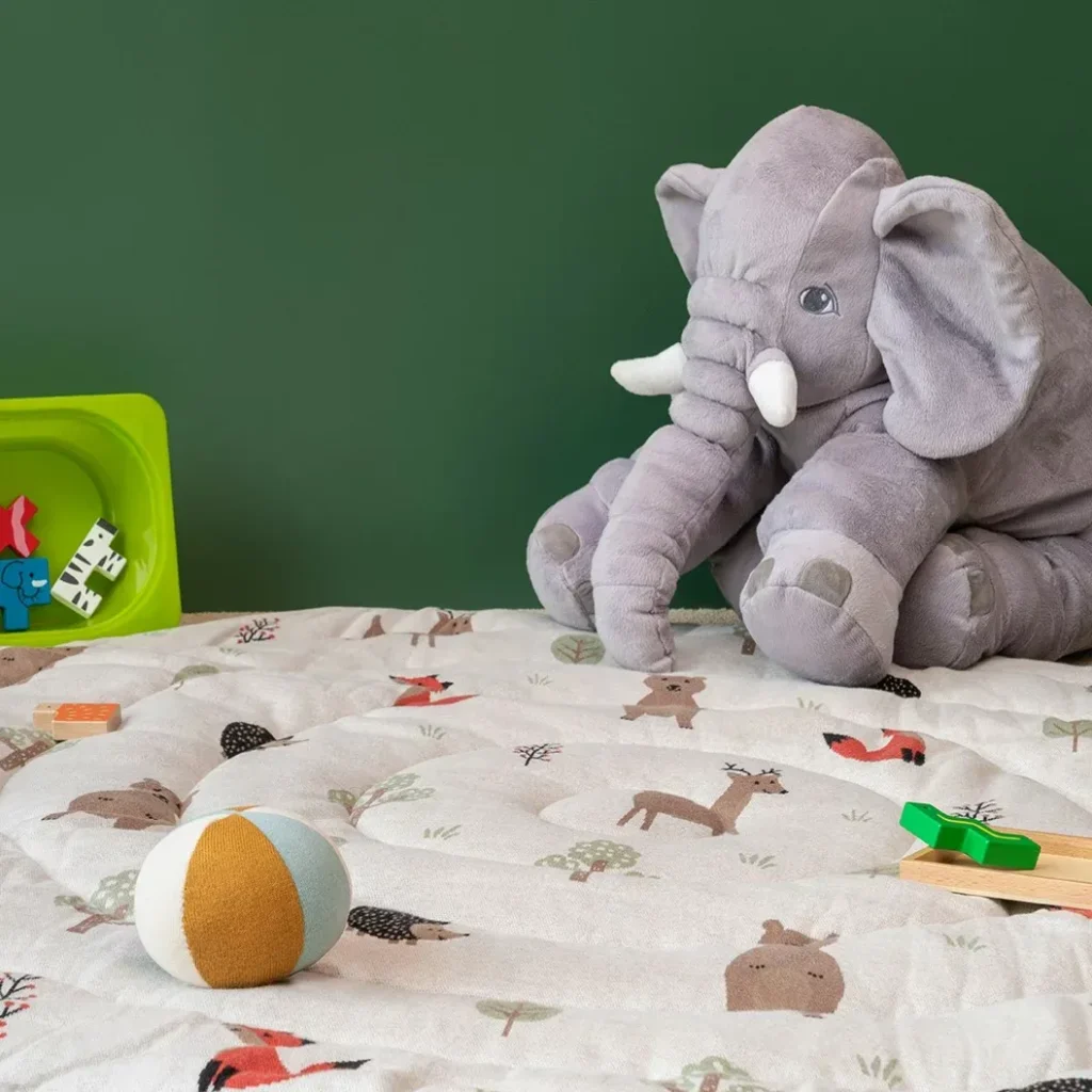 Soft gray elephant plush on play mat with toys