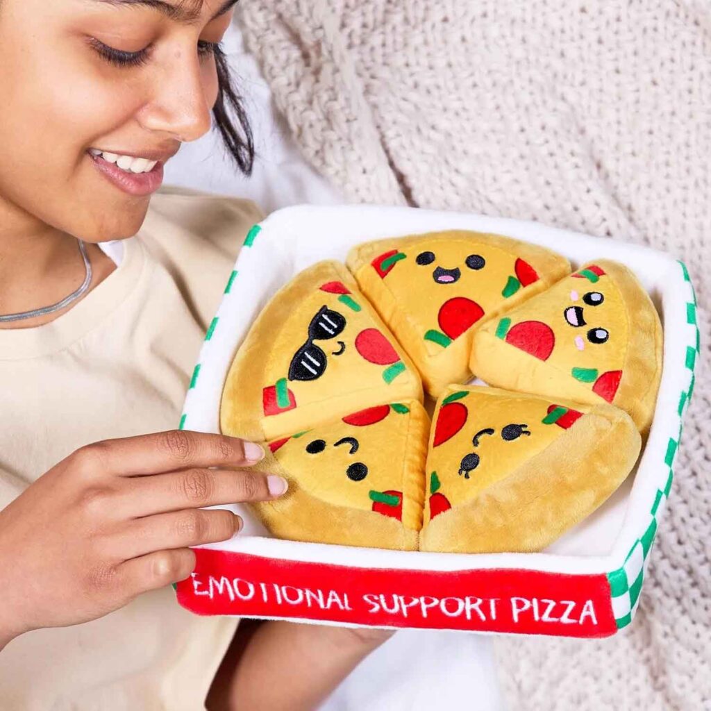 Smiling girl holding a plush pizza box labeled “Emotional Support Pizza” with five cute cartoon slice toys inside