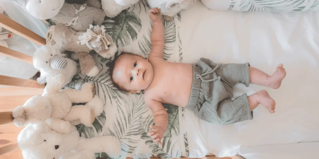 Baby lying in crib surrounded by soft plush animals on tropical leaf bedding in a cozy nursery