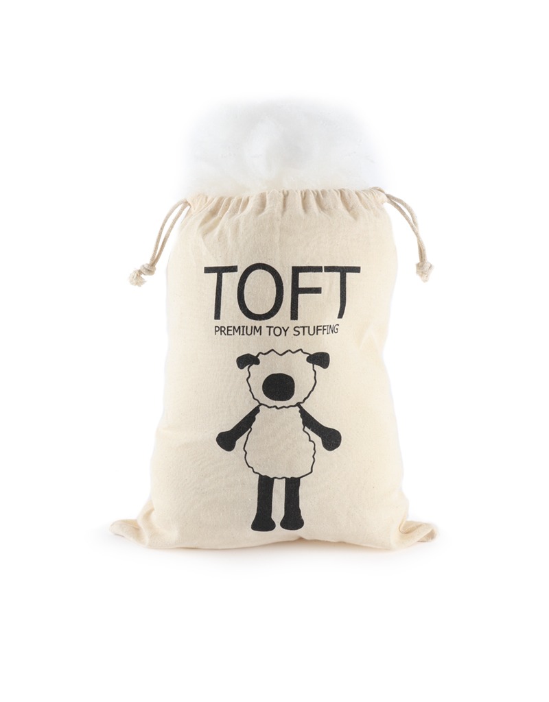 Un sacchetto con cordoncino in cotone etichettato "TOFT Premium Toy Stuffing" riempito con fibra di poliestere bianca per peluche.
