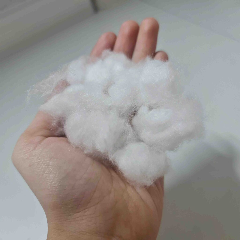 Hand holding soft white polyester fiberfill used for toy stuffing and cushions.
