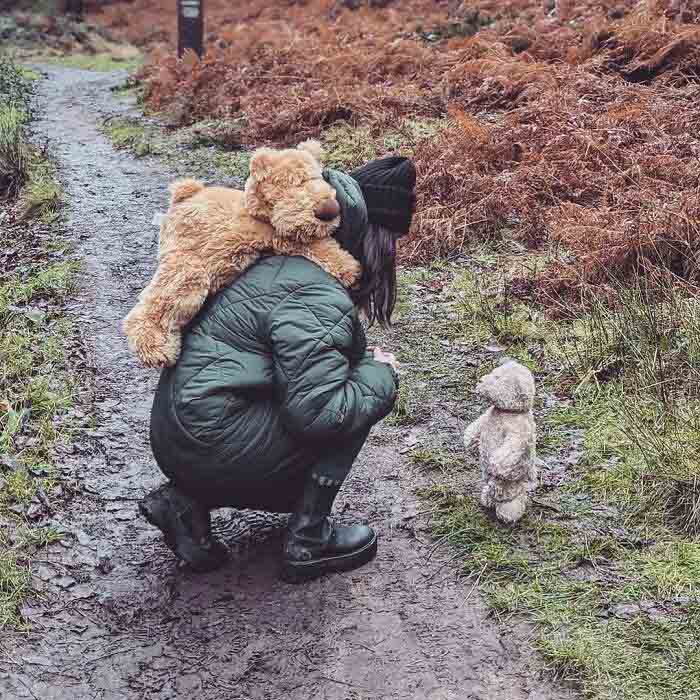 Woman crouching with teddy bears on muddy forest path