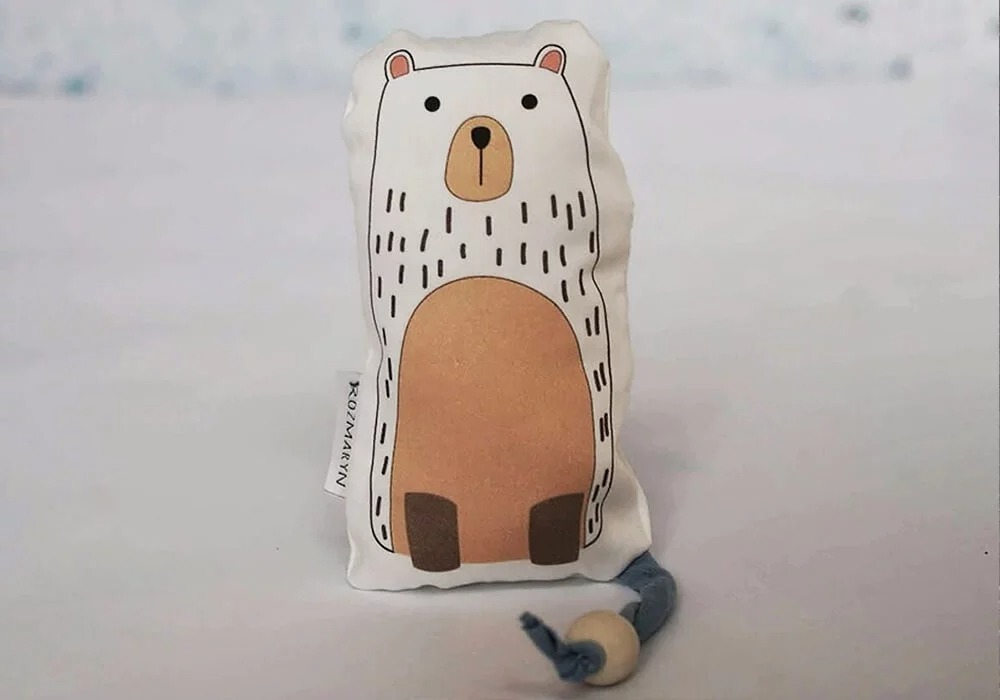 Pequeno peluche minimalista com ilustração de um urso e laço de tecido com conta de madeira.