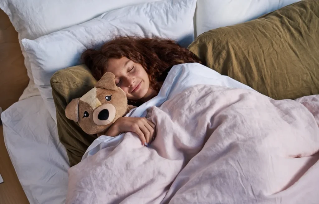Woman cuddling plush bear while sleeping in bed