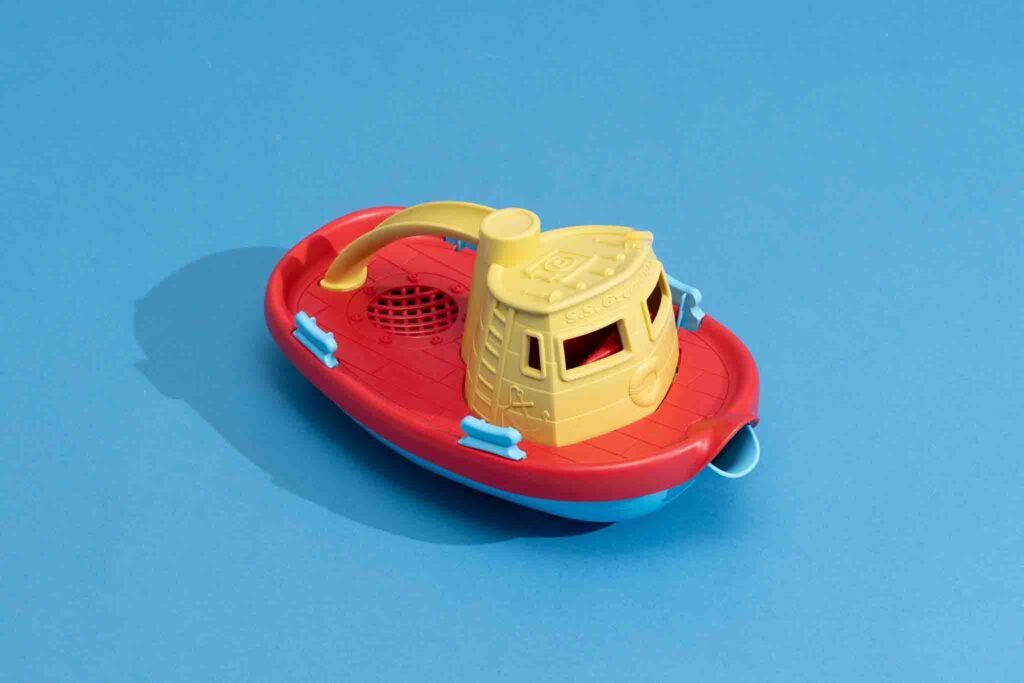 Rode, gele en blauwe plastic speelgoedboot op blauwe achtergrond, ideaal voor waterspelen