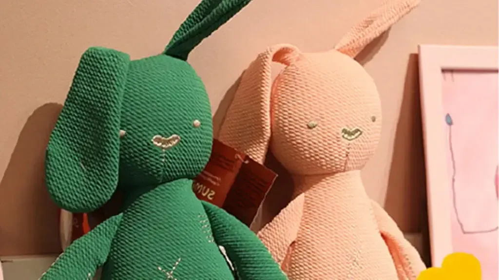 Green and pink knitted bunny plush toys sitting beside wall decor.