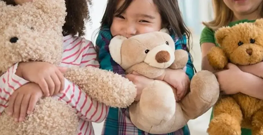 Drei Kinder halten und umarmen weiche Teddybären, lächeln und tragen bunte Kleidung.