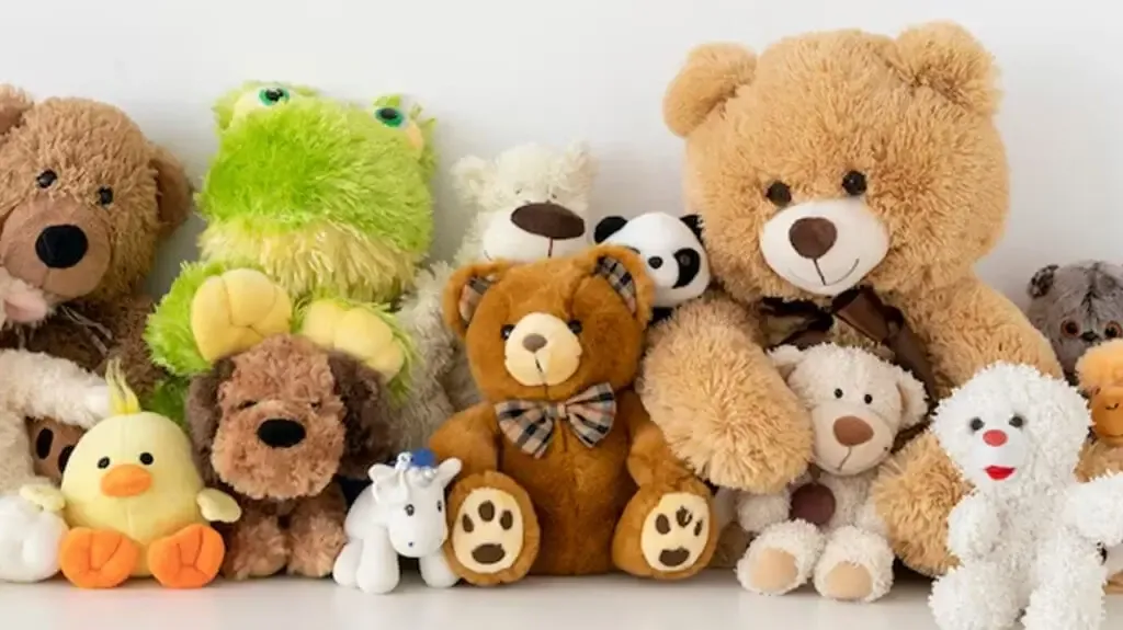 A colorful variety of plush toys including teddy bears, a frog, a duck, a panda, and more, all arranged side by side on a shelf.