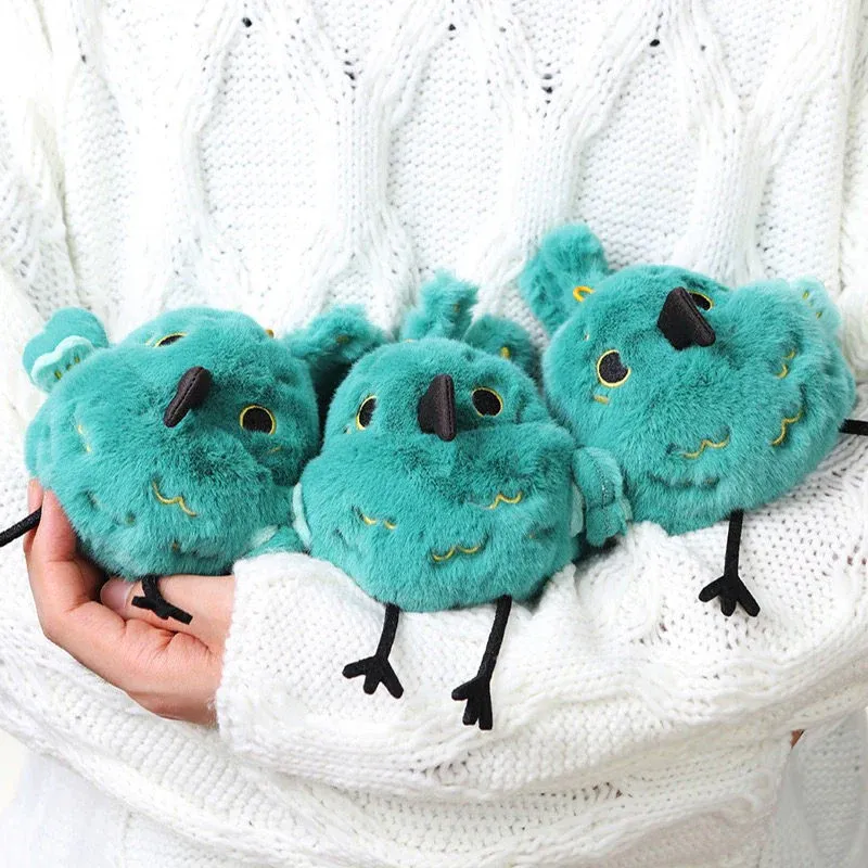 Three small green plush birds held in hands wearing white sweater.