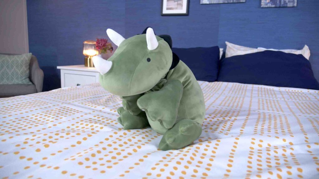 Green dinosaur plush toy sitting on bed