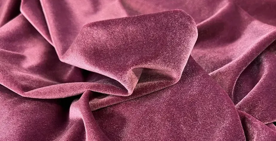 Grande plano de um luxuoso tecido de veludo cor-de-rosa com dobras suaves e brilho.
