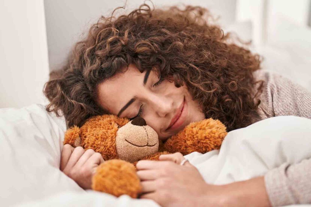 Smiling woman hugging soft teddy bear in bed
