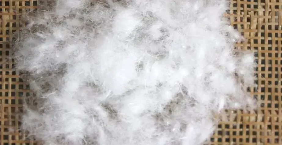 Primo piano di un materiale di imbottitura bianco e morbido utilizzato per riempire i peluche, posato su una superficie tessuta.