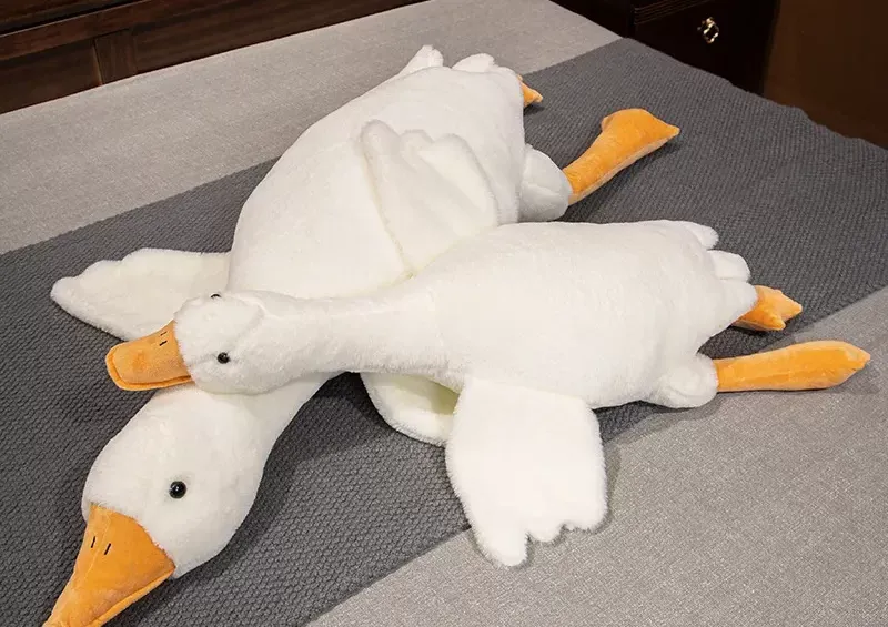 Pair of white goose plush slippers with orange beaks and feet on gray surface.