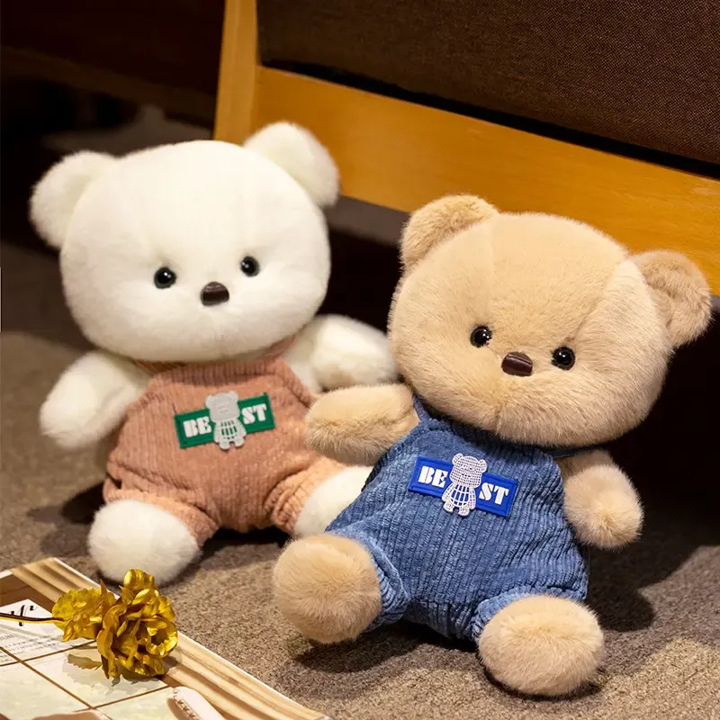 Two soft plush bears wearing overalls sitting on carpet next to a golden flower.