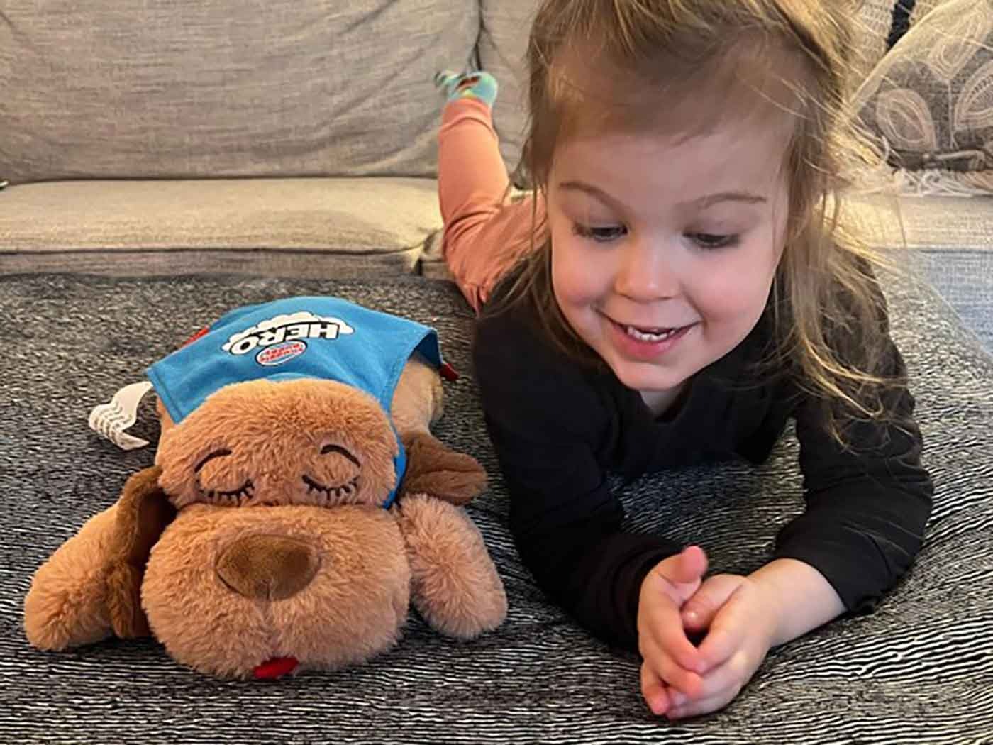 Child laying beside hero-themed dog plush toy