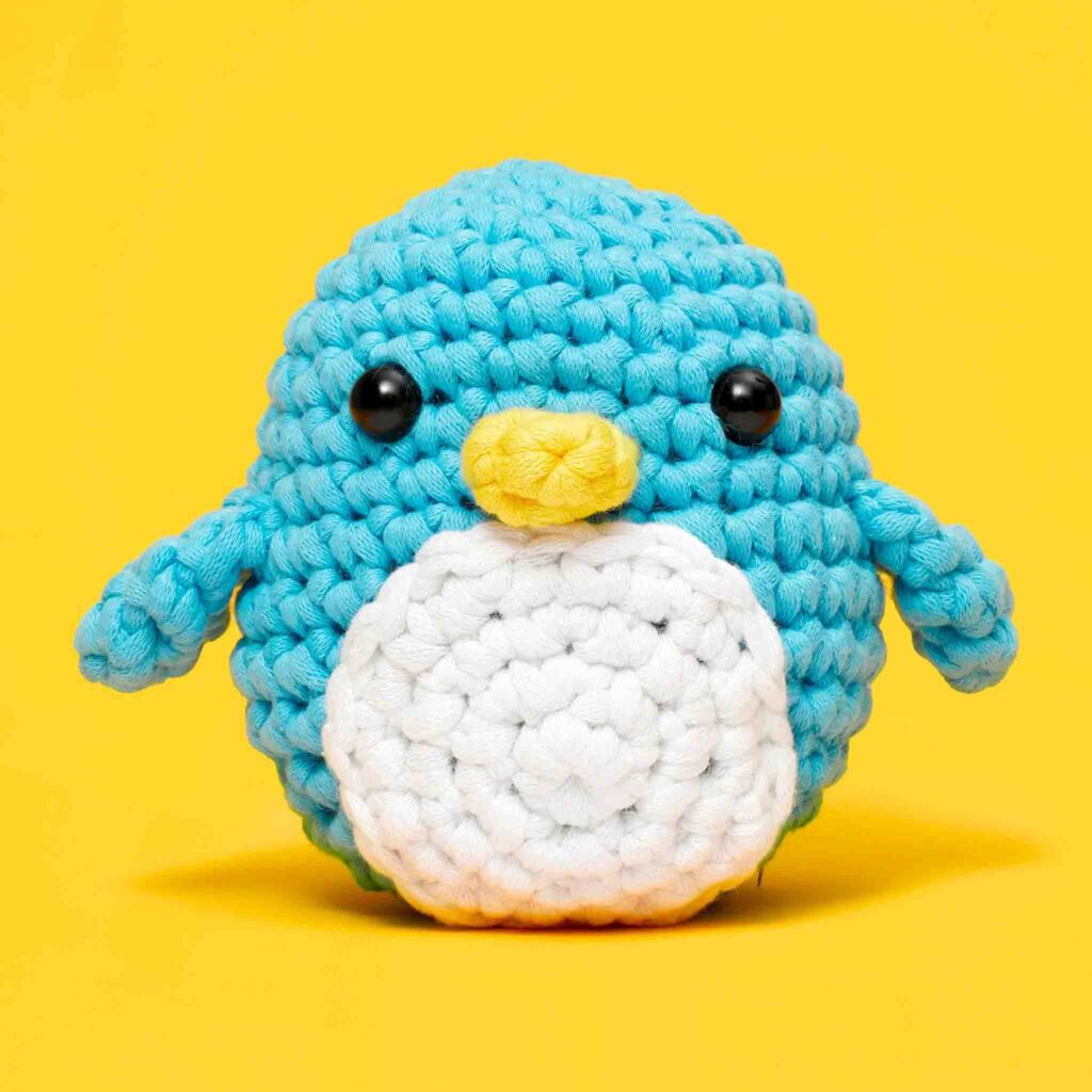 Peluche pinguino blu fatto a mano all'uncinetto con pancia bianca e becco giallo su sfondo giallo