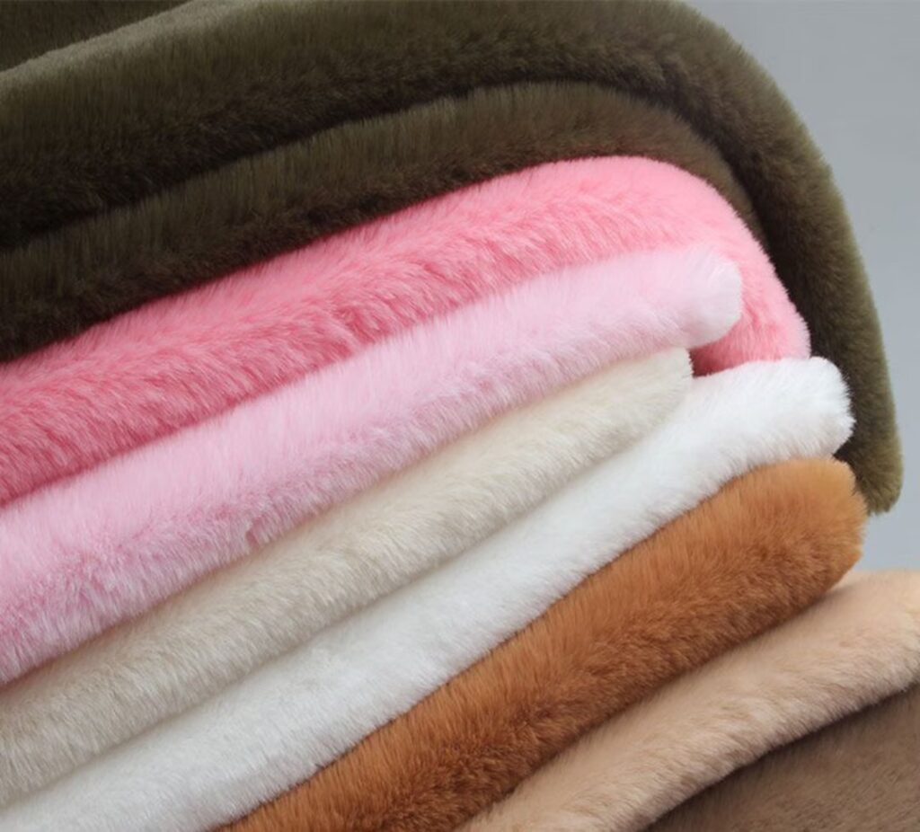 Stack of soft faux fur fabric rolls in various colors, including brown, pink, white, and beige, plush textile materials used for stuffed animals or clothing, close-up of fluffy and smooth synthetic fabric, cozy and colorful fabric swatches.