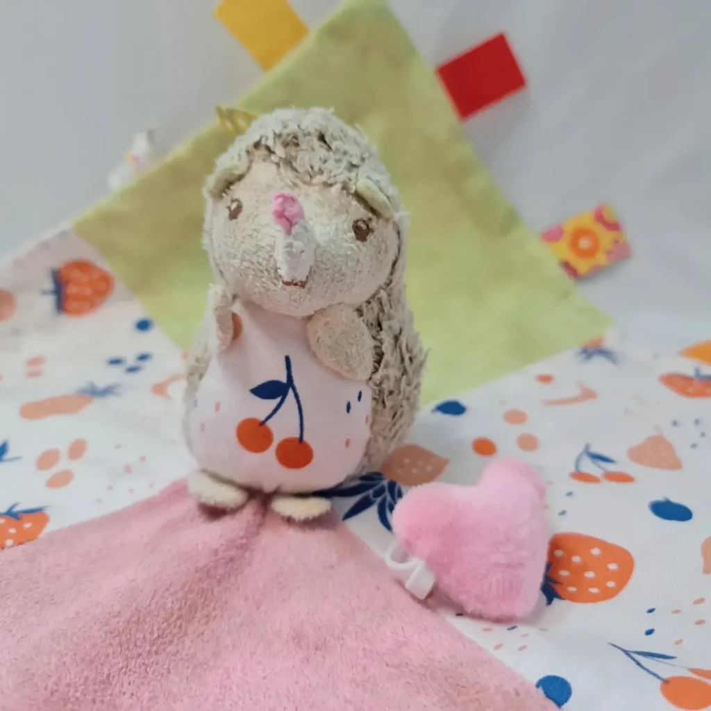 Plush hedgehog with pink blanket and colorful background.