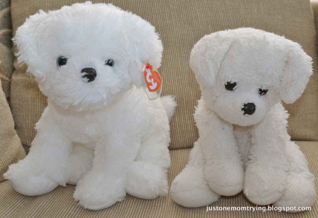 Two white stuffed puppy toys sitting on a beige couch, one new with a Ty tag and one older and worn.