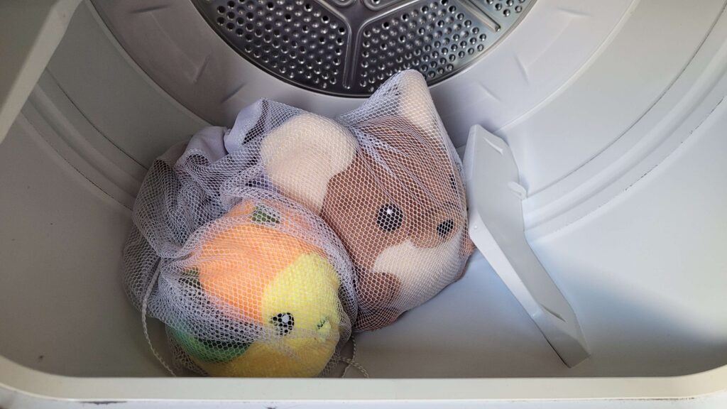 Two plush toys inside mesh laundry bags placed in a dryer drum for gentle drying.