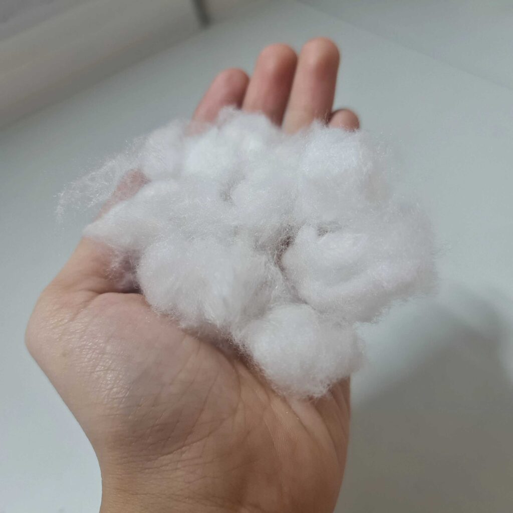 Close-up of hand holding soft white polyester fiberfill stuffing, fluffy synthetic material for plush toys or pillows, lightweight and smooth texture, used for toy filling or cushions, toy manufacturing supplies, stuffing fiber material, clean fiber in palm.