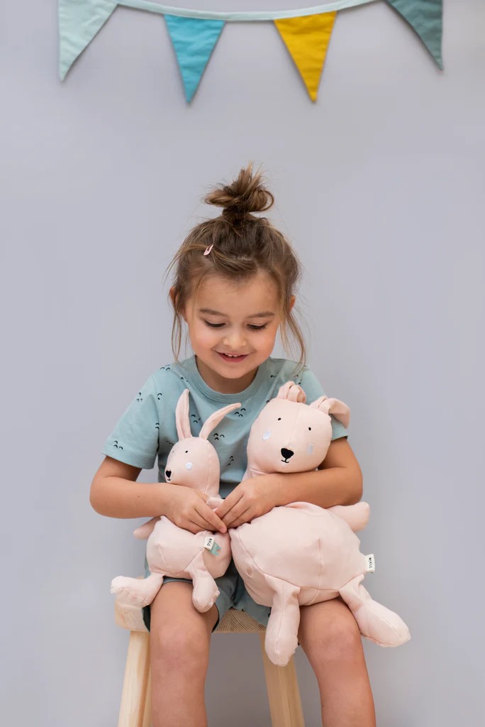 Little girl holding two light pink plush animals on her lap