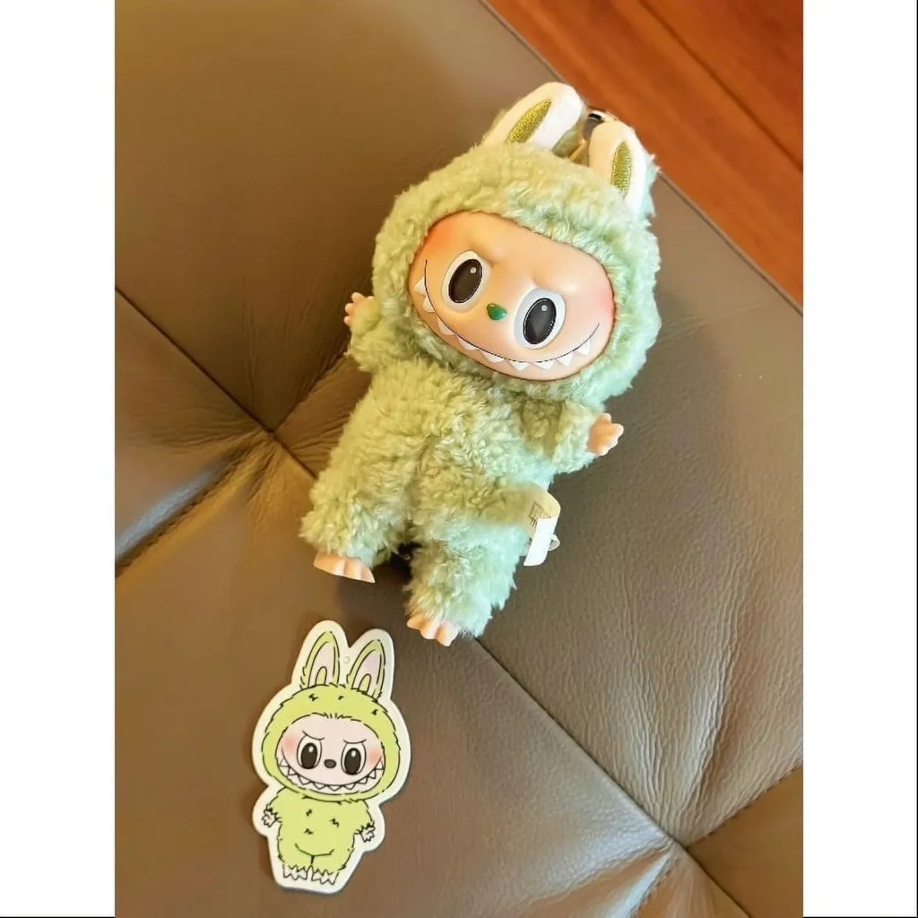 Green Labubu plush toy with matching keychain on leather surface.