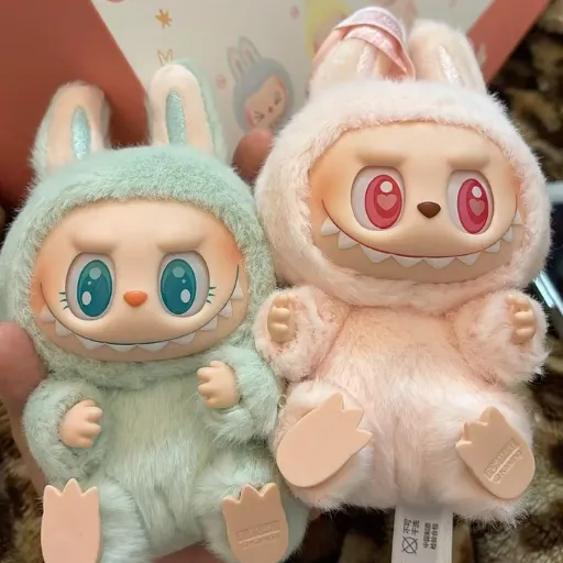Two Labubu plush dolls in pastel green and pink fuzzy costumes with big eyes.